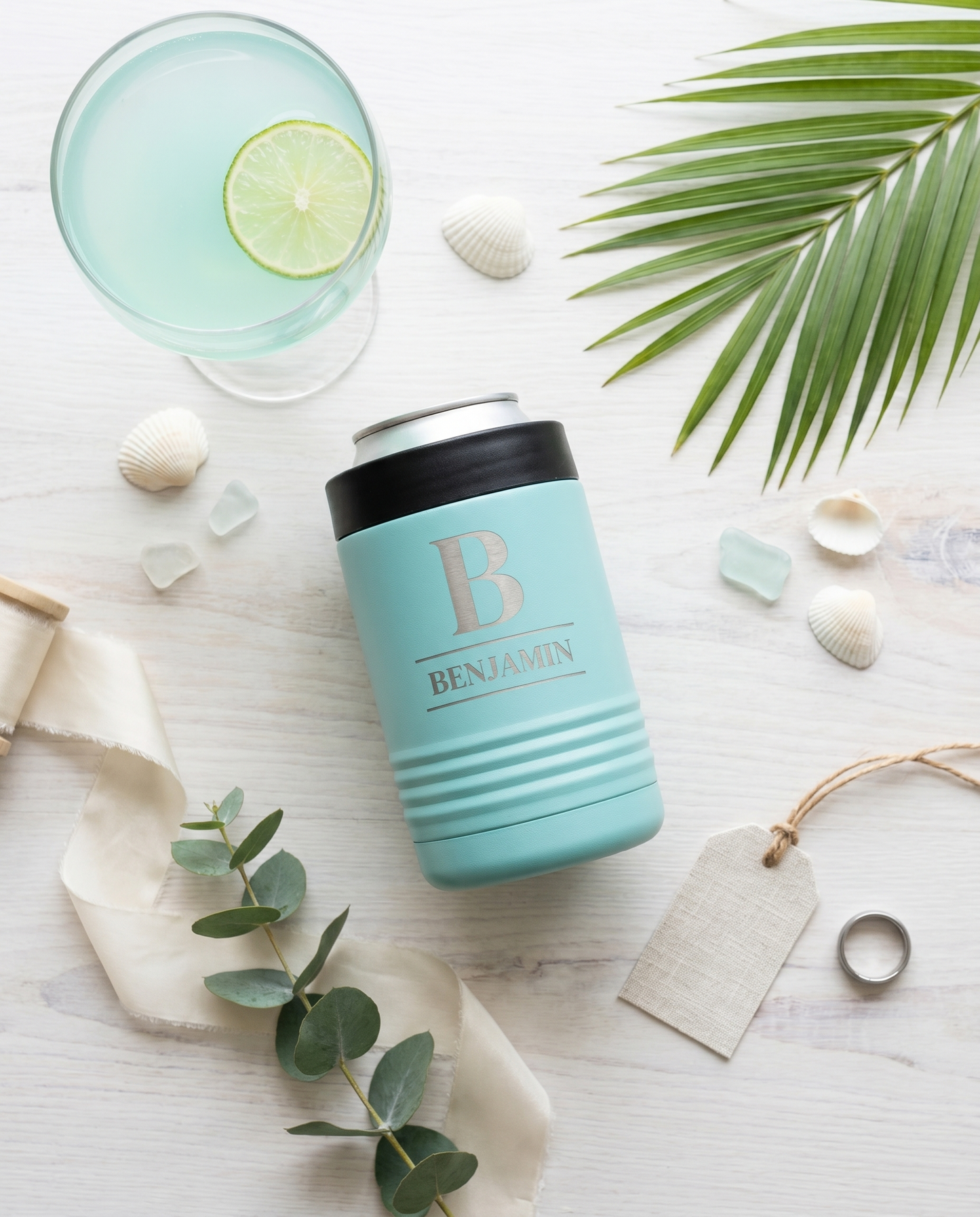Personalized teal stainless steel insulated can cooler flat lay with paloma cocktail and palm frond