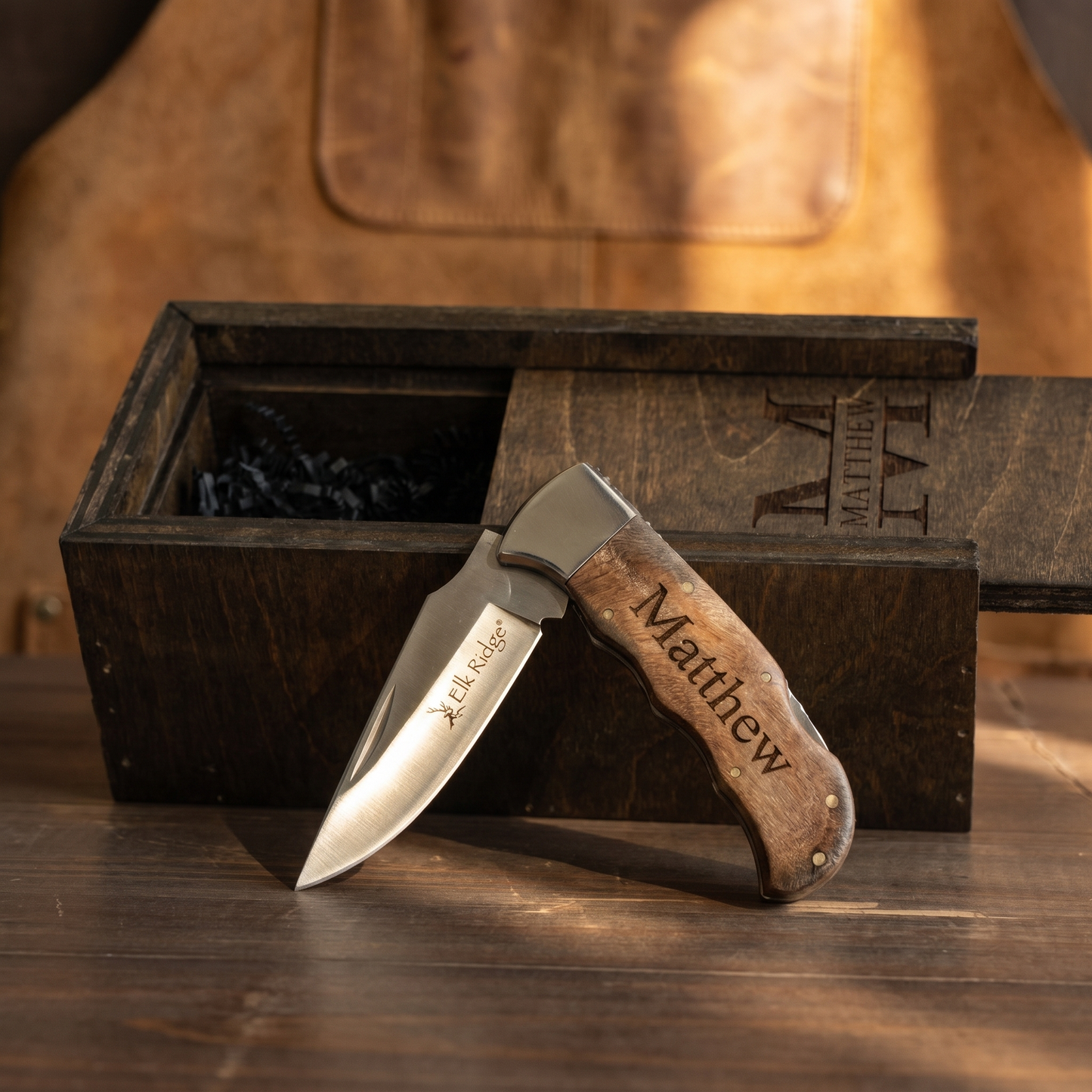 Personalized burl wood pocket knife blade detail with leather apron backdrop and matching wooden gift box