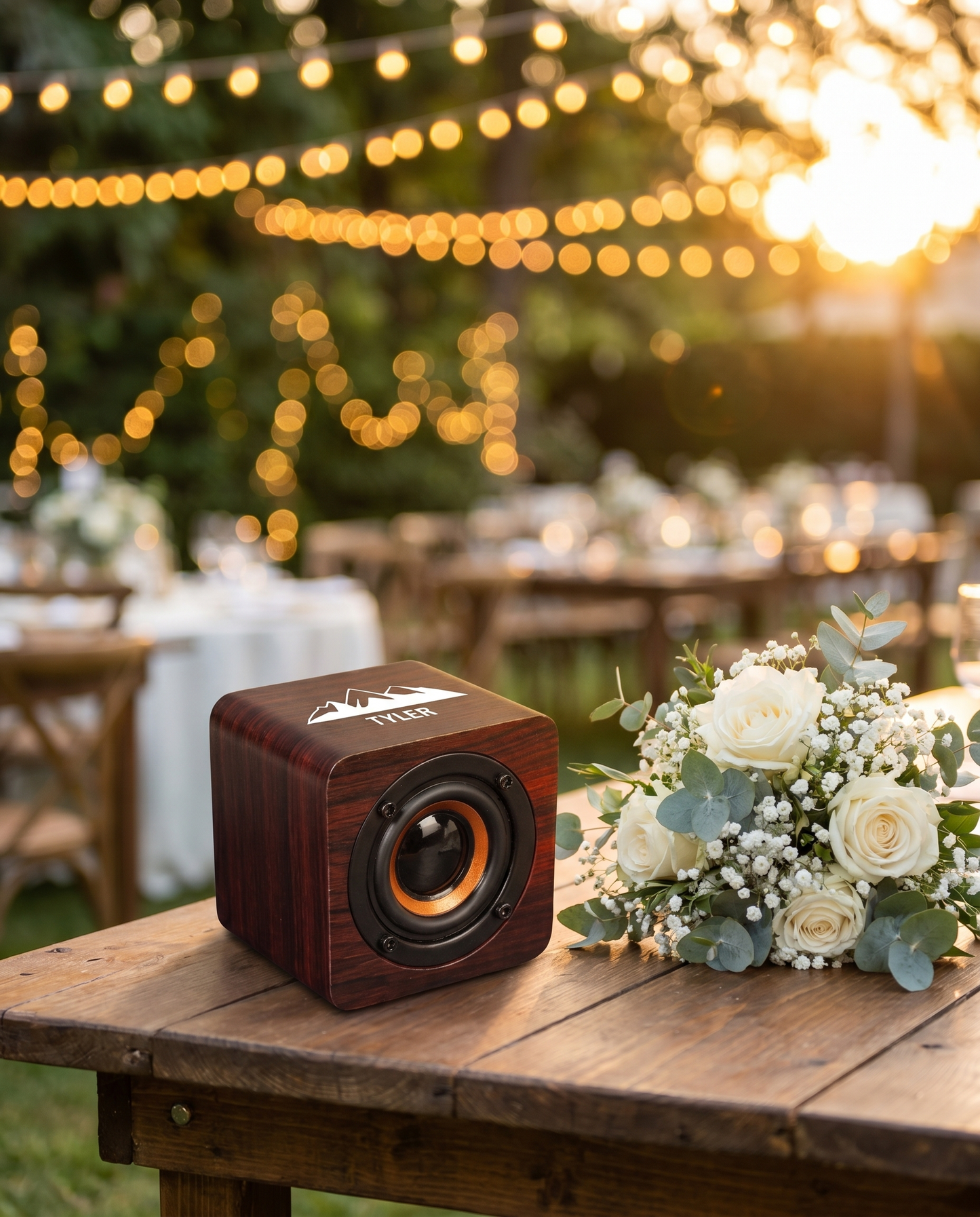 Cherry wood Bluetooth speaker at outdoor wedding reception, golden hour with string lights