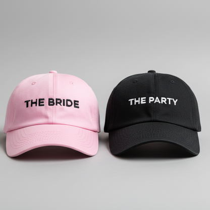 Pink and black hats labeled 'The Bride' and 'The Party' on a brick surface.