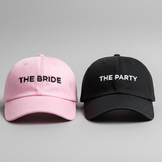 Pink and black hats labeled 'The Bride' and 'The Party' on a brick surface.